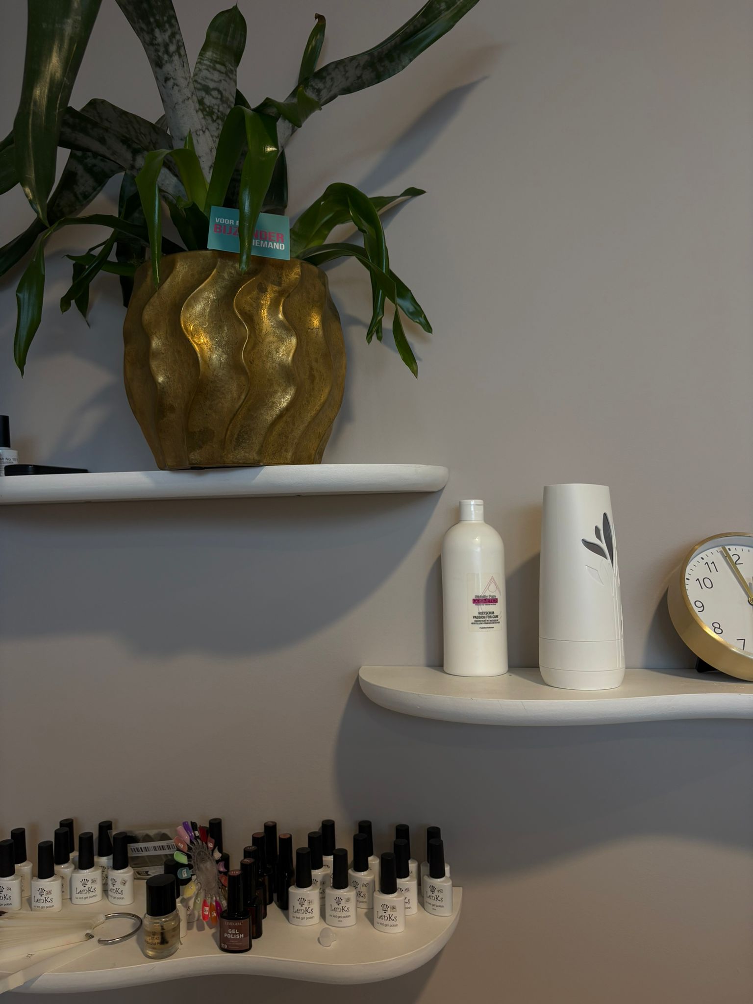 Productschap met gellakkleuren, voetscrub en een gouden plantenpot in de salon